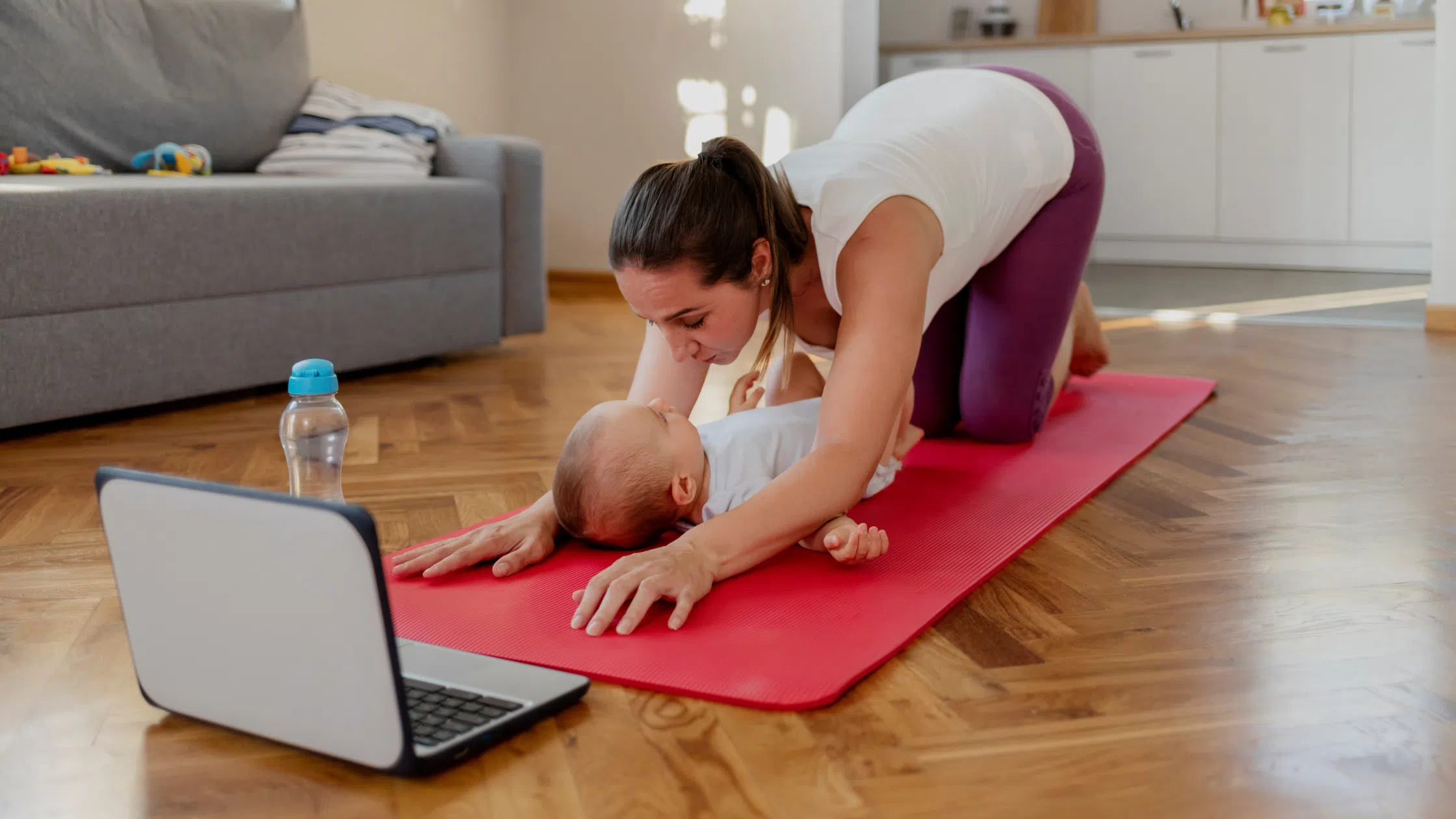 A mother doing post-pregnancy skin tightening exercises at home on a yoga mat, bonding with her baby nearby.